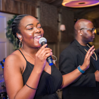 Smiling female singer performing live with musician in warmly lit indoor music venue.