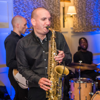 Jazz trio performing live with saxophone, guitar, and drums at cozy indoor venue.