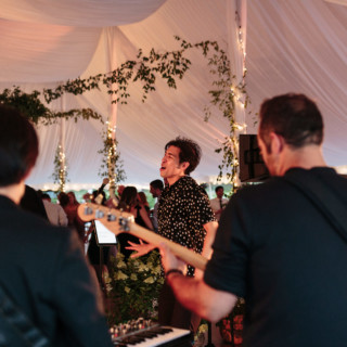 Live band performing at elegant wedding reception under white tent with lights and greenery.