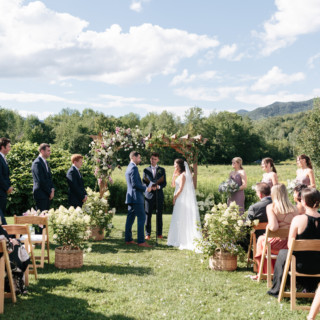 Couple exchanging vows under floral arch at scenic outdoor wedding in Stowe, Vermont.