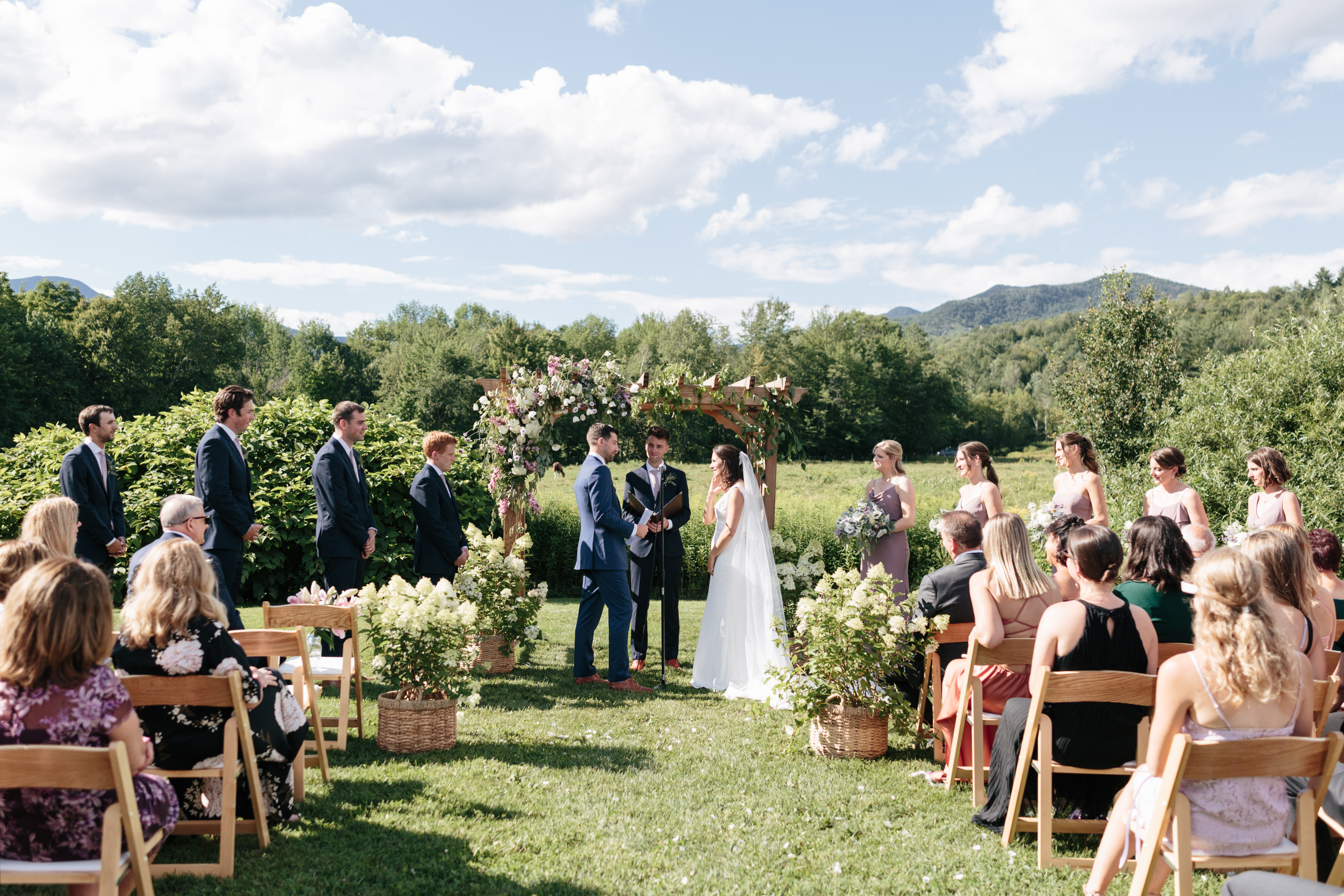 Couple exchanging vows under floral arch at scenic outdoor wedding in Stowe, Vermont.