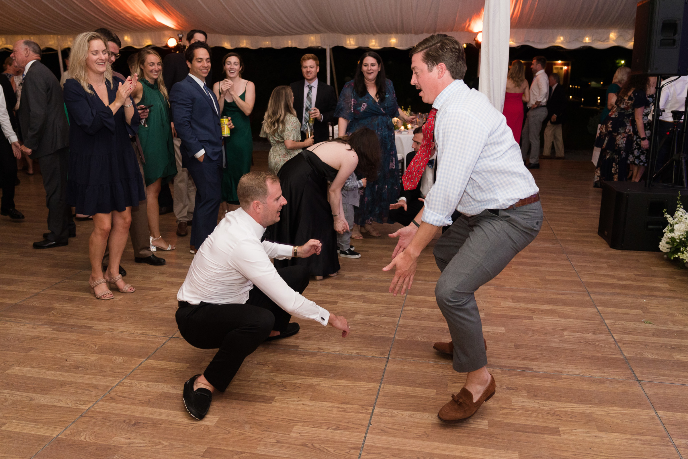 Two men dancing joyfully at elegant Vermont wedding reception under glowing tent lights.