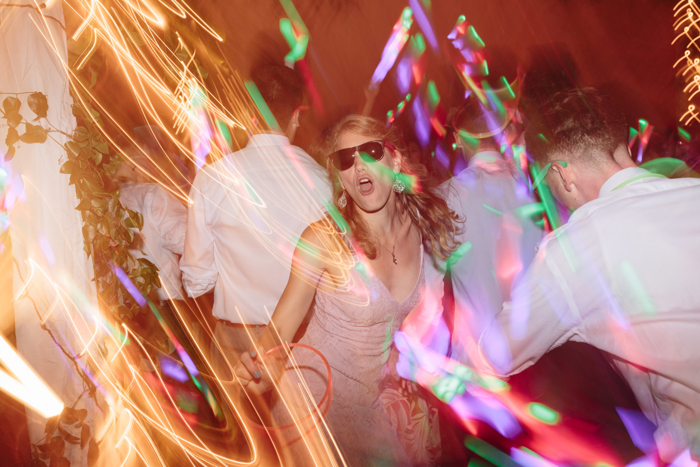Woman dancing in pink dress under colorful lights at lively Stowe wedding party.