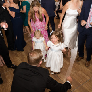 Two young flower girls dancing joyfully with guests at an elegant Vermont wedding reception.