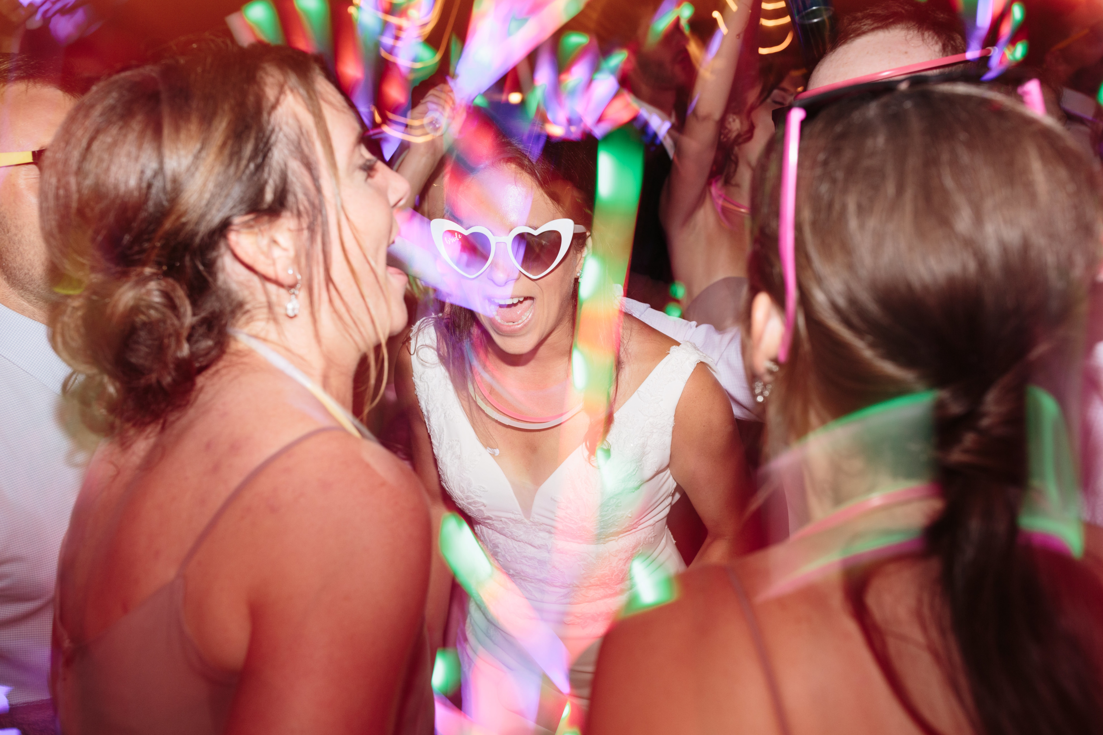 Bride dancing with friends under colorful neon lights at lively Topnotch Resort wedding in Stowe.