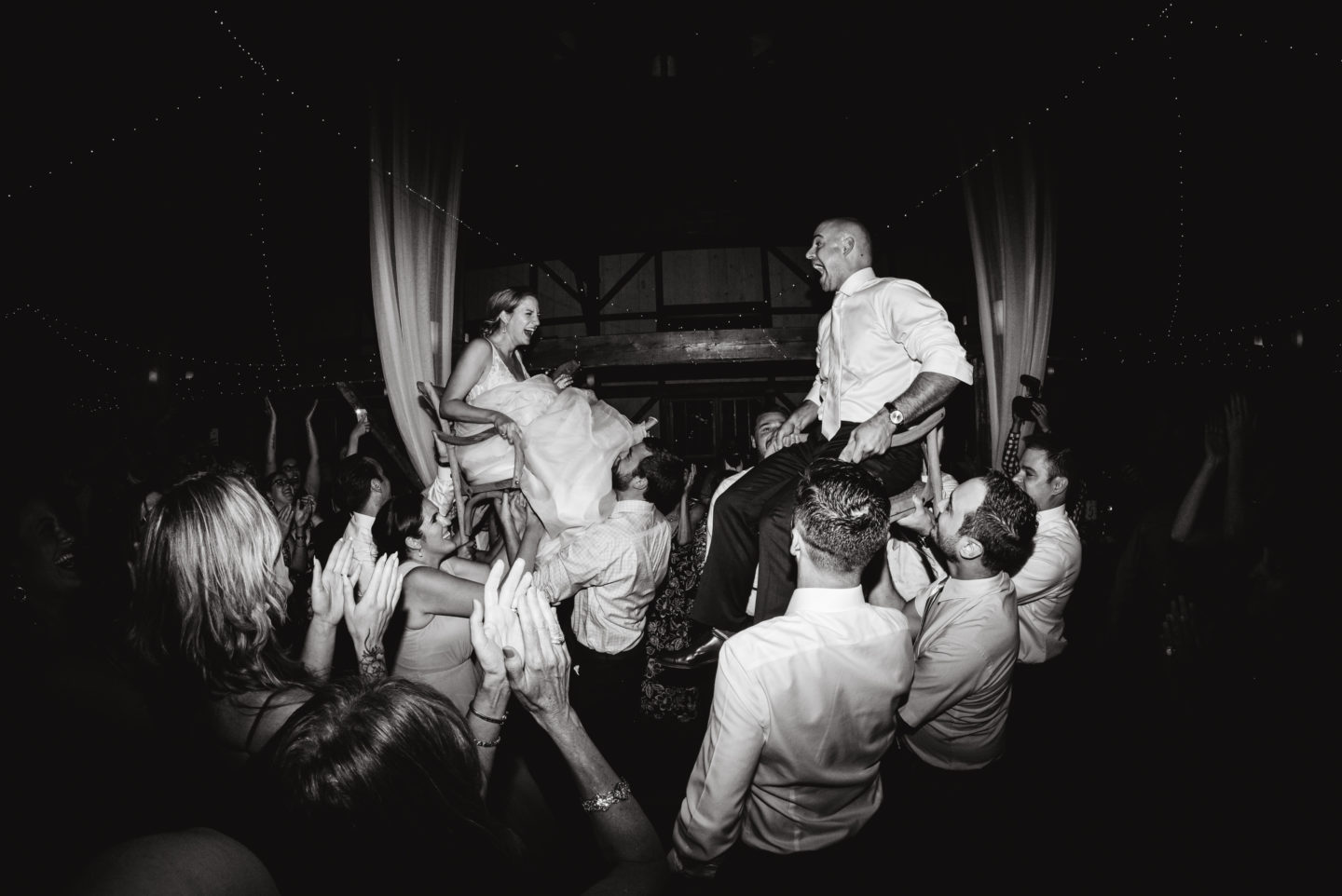 Bride and groom lifted on chairs during lively Hora dance at rustic Valley View Farm wedding.