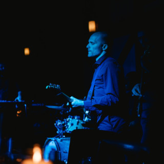 Guitarist performing under blue stage lights in an intimate, candlelit live music setting.