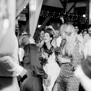 Bride dancing joyfully with friends at rustic barn wedding reception in black and white.
