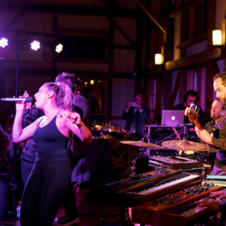 Energetic live band performance with passionate singer under purple and amber lighting in rustic venue.