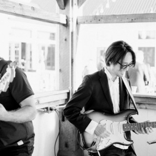 Two guitarists performing live at a rustic sunlit venue in Haydenville, Massachusetts.
