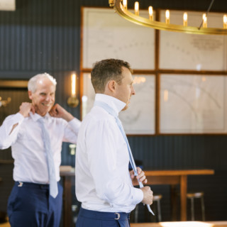 Groom and groomsman adjusting blue ties before wedding at Valley View Farm in Massachusetts.