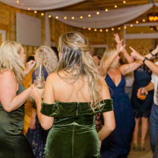 Guests dancing at a rustic barn wedding reception in Sebago, Maine under warm string lights.