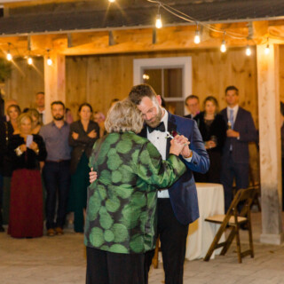 Groom dancing with his mother under warm string lights at rustic Autumn Lane Estate wedding.