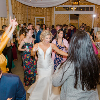 Bride dancing joyfully with guests at rustic barn wedding reception in Sebago, Maine.