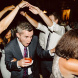 Man dancing through raised arms tunnel at joyful Boston Public Library wedding reception.