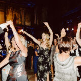 Guests dancing joyfully at elegant Boston Public Library wedding reception under warm golden lights.
