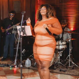 Female singer in orange dress performing with live band at elegant indoor venue.