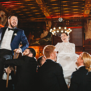 Bride and groom lifted on chairs during joyful Hora dance at Boston Public Library wedding.