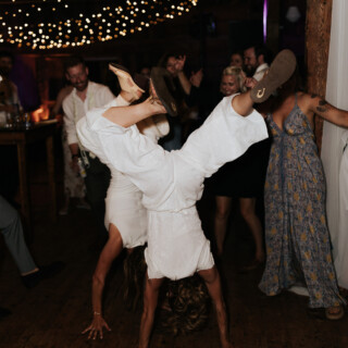 Woman doing a handstand on rustic barn dance floor during joyful wedding celebration in Maine.