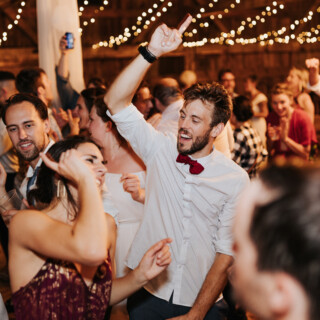 Guests dancing under warm string lights at a joyful rustic barn wedding in Maine.
