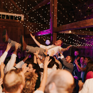 Guests lift a joyful groom during a lively barn wedding celebration in New Gloucester, Maine.