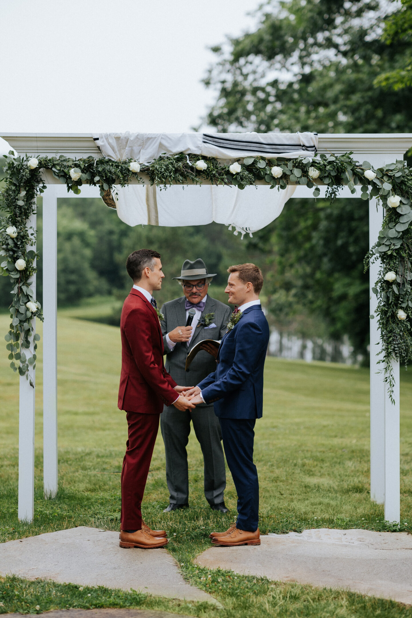 Two grooms exchange vows under a white floral arch at Cunningham Farm in Maine.