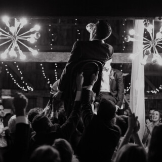 Two grooms lifted during joyful Hora dance at Cunningham Farm wedding in New Gloucester, Maine.