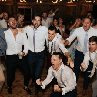 Groom and friends singing joyfully on the dance floor at a lively Maine wedding.