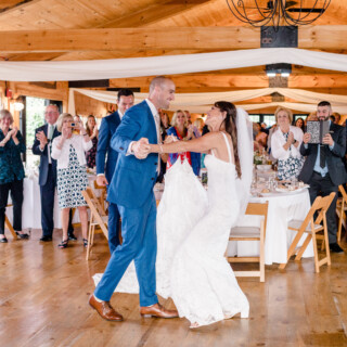 Bride and groom dancing joyfully at rustic Vermont wedding with cheering guests and warm wood décor.