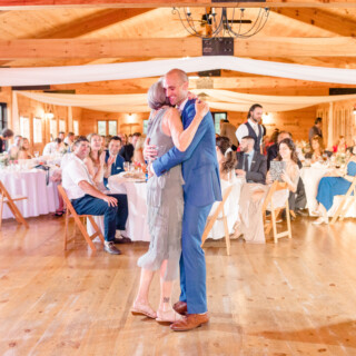 Groom and mother share emotional dance at rustic Vermont wedding in warm golden light.