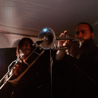 Passionate live jazz performance with trumpet and trombone under warm evening lights.