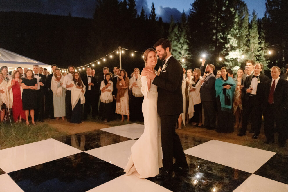 Bride and groom first dance under string lights at romantic forest wedding in Big Sky Montana