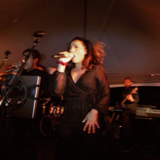 Female singer performing passionately on stage under warm orange lights at an intimate live concert.