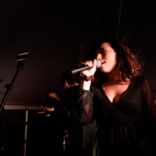 Female singer performing passionately on stage under dramatic lighting at live music event.