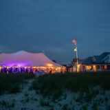 Twilight beachfront wedding celebration in Nantucket with glowing tent and charming coastal home.