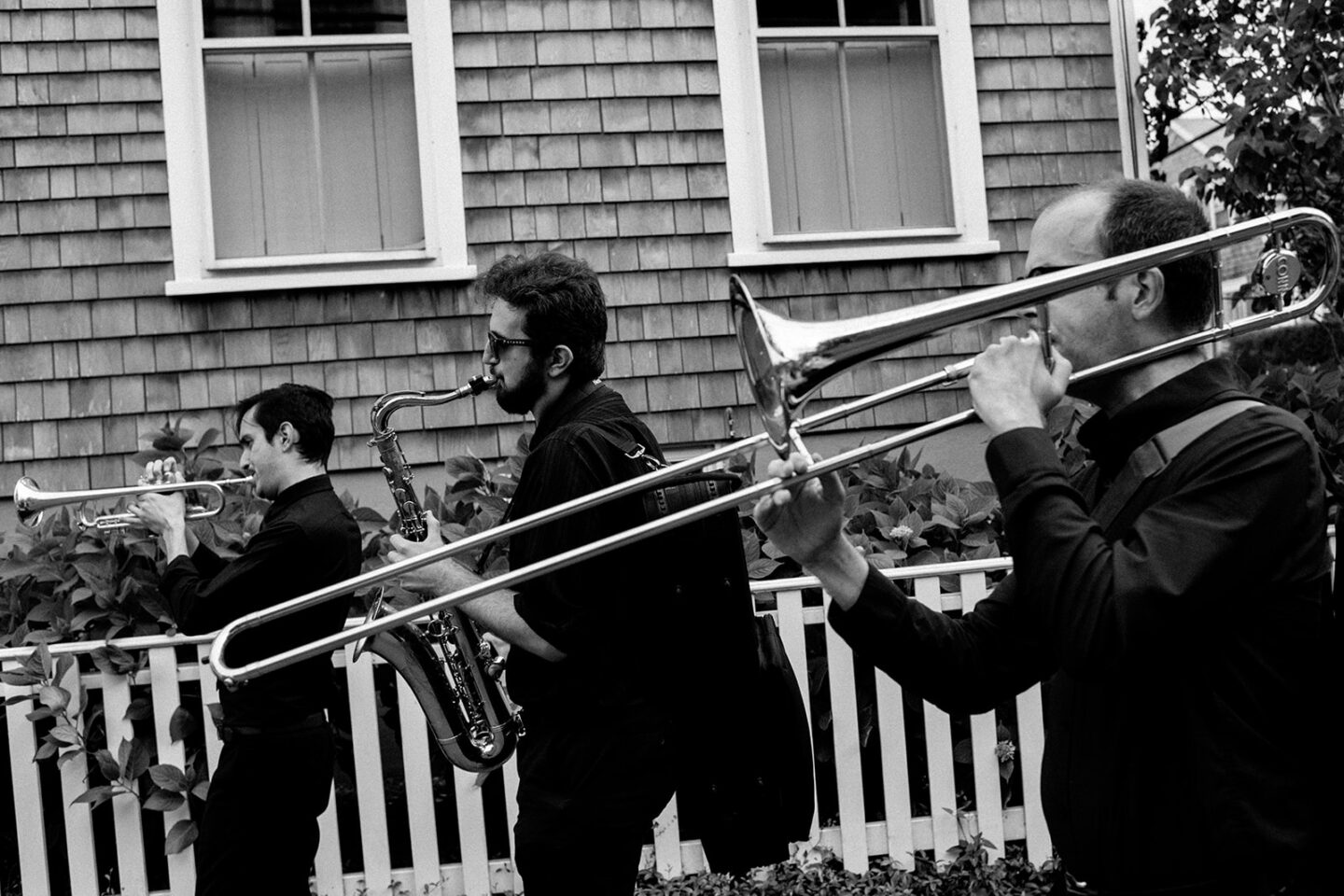 Black and white photo of three brass musicians performing outside a Nantucket home.