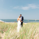Bride and groom holding hands on a sandy dune path overlooking the ocean in Nantucket.