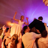 Bride and groom lifted by guests during joyful Nantucket wedding celebration under glowing tent lights.