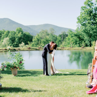 Bride and groom kiss by a scenic pond during a Vermont countryside outdoor wedding ceremony.