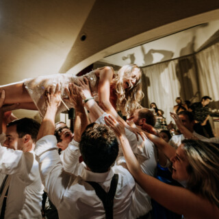 Bride lifted joyfully by guests during lively wedding celebration at Bar Harbor Club, Maine.
