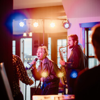 Female jazz singer and saxophonist performing live in a warm, intimate lounge setting.