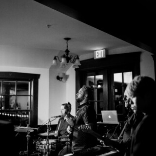 Black and white live band performance in an intimate, warmly lit wedding setting.