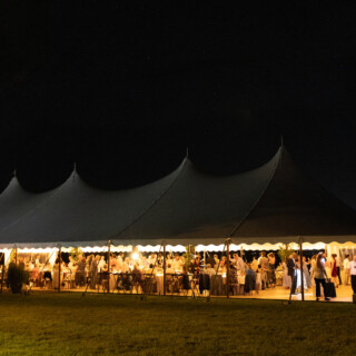 Elegant outdoor wedding reception under glowing sailcloth tent at night in Bristol, Rhode Island.