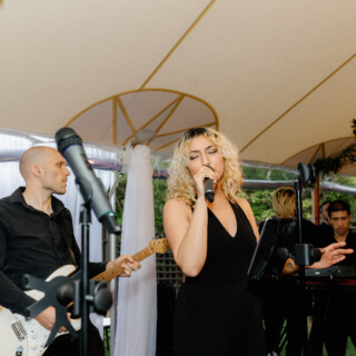 Female singer performing with live band under greenery canopy at elegant Willowdale Estate wedding.