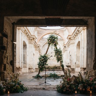 Romantic wedding ceremony with floral arch in ancient stone ruins, blending history and modern elegance.