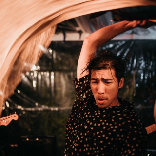 Guitarist swinging instrument overhead during energetic live rock concert under warm amber stage lights.