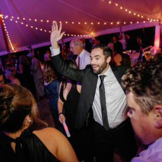 Joyful wedding guests dancing under glowing string lights at Bradley Estate in Canton, Massachusetts.