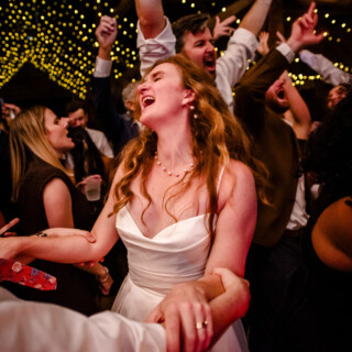 Bride laughing and dancing under golden string lights at joyful Cunningham Farm wedding celebration.