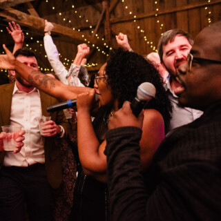 Wedding band performing in rustic barn as guests celebrate under warm string lights in Maine.