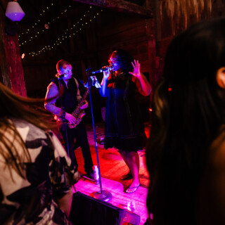 Live band performing at rustic barn wedding with vibrant lighting and engaged audience in Maine.